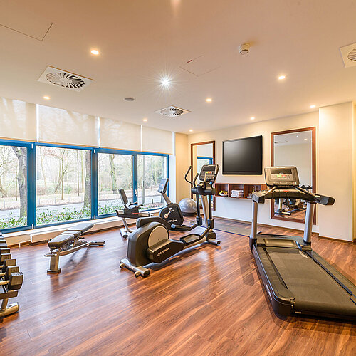 Modern fitness center with a view at Maritim Hotel Bremen, featuring treadmill, dumbbells, and workout machines.