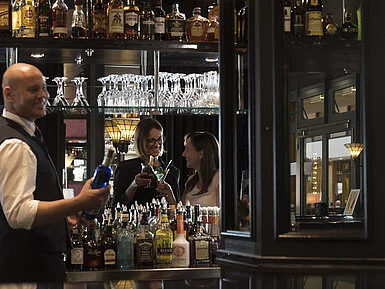 Happy guests enjoying cocktails at the bar of Maritim Hotel Dresden, served by a friendly bartender.