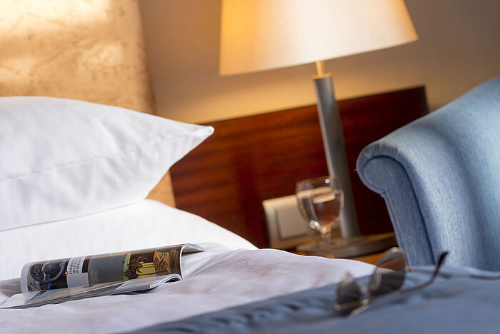  Close-up of a hotel room at Maritim Hotel Fulda with bed, magazine, glasses, and a glass of water on the nightstand.
