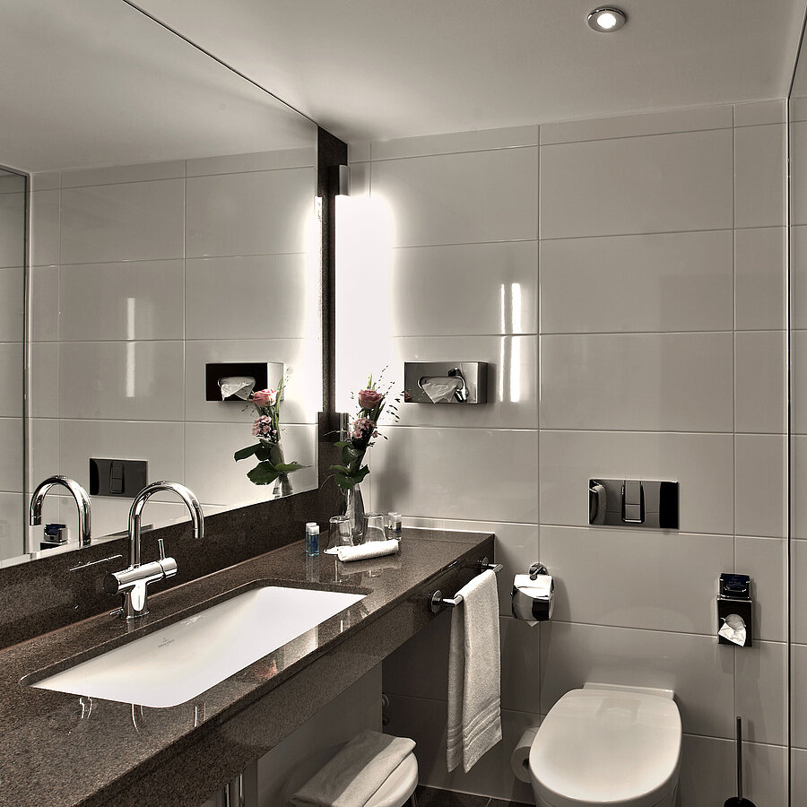 Modern bathroom at Maritim Hotel Cologne with bathtub, large mirror, and stylish lighting in neutral tones.