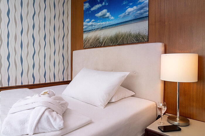 Queen-size bed in the Superior Queen room with bedside lamp and bathrobe