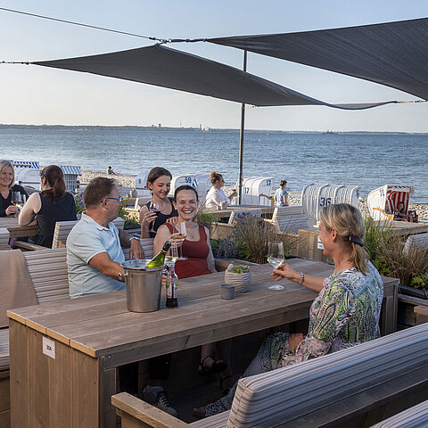 Group of guests at the beach bar of Maritim Seehotel Timmendorfer Strand enjoying drinks with sea view and beach chairs.