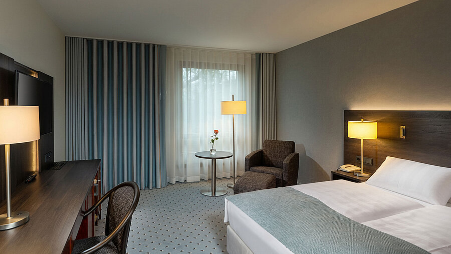 Classic Queen room with queen-size bed, seating area, desk, warm lighting and classic interior design.