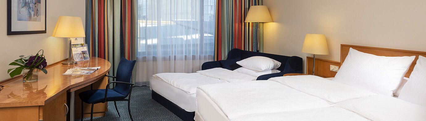 Classic family room at Maritim Hotel Frankfurt with double bed, sofa bed, desk, and colorful curtains.