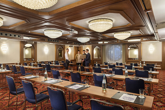 The Cologne Hall with elegant chandeliers and seating rows in a classic conference room setting, ready for a meeting.