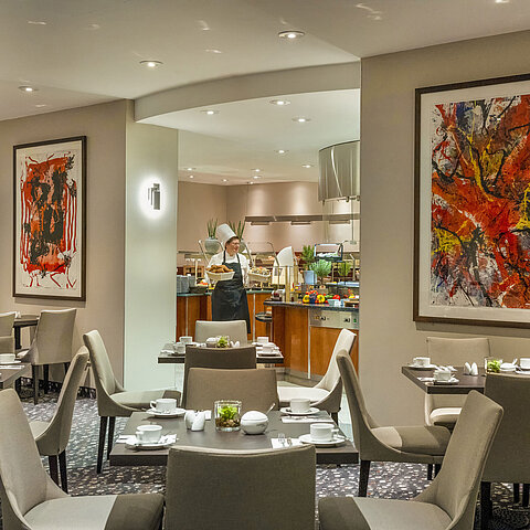 Restaurant at Maritim proArte Hotel Berlin with modern art on walls, set tables, and a chef at the buffet.