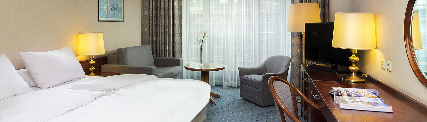 Family room Bright family room at Maritim Hotel Cologne with double bed, desk, TV, armchairs, and large windows with curtains.