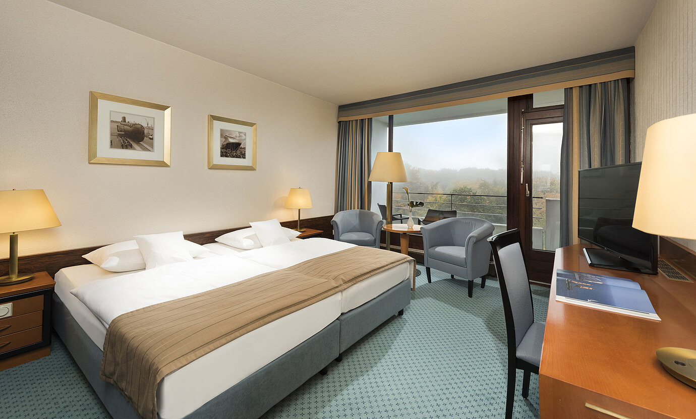 Classic room at the Maritim Hotel Kiel with large double bed, seating area, desk and balcony with a view of the countryside.
