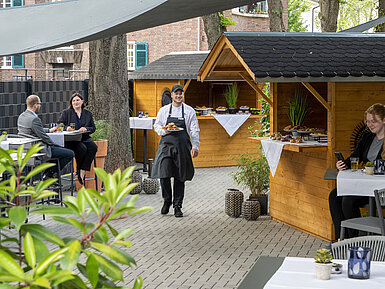 Waiter serving food at an event on the terrace of the Maritim Hotel Darmstadt with wooden huts