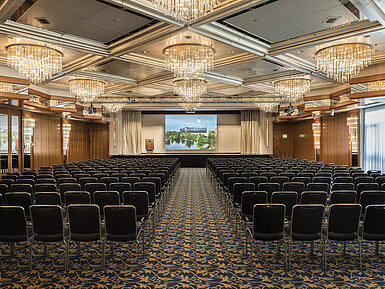 Elegant event hall with crystal chandeliers, row seating, and a large stage at Maritim Hotel Hannover.