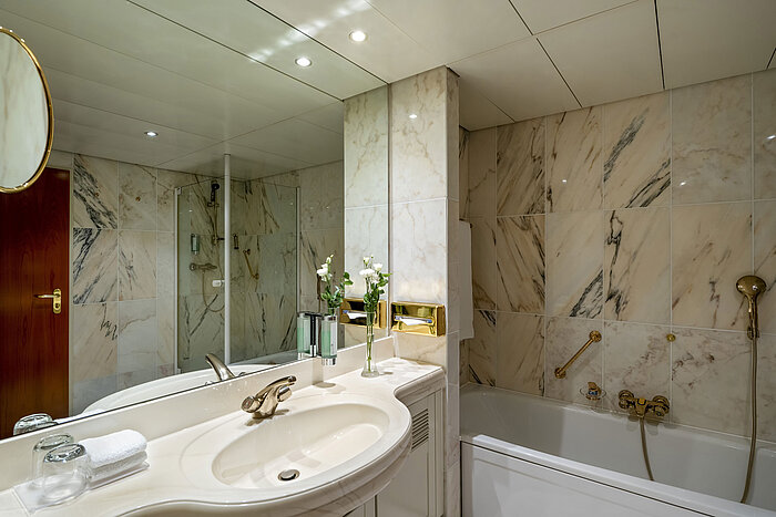 Modern bathroom at Maritim Hotel Hannover with bathtub, glass shower, and marble walls.