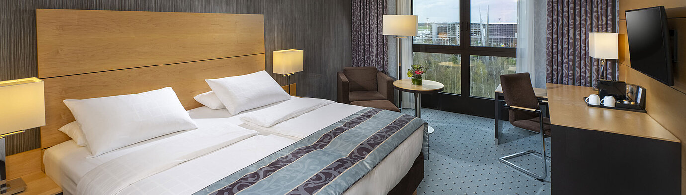 Modern superior room at Maritim Hotel Düsseldorf with a large bed, desk, and city view.