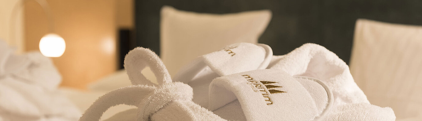 Bathrobe White bathrobe and slippers with Maritim logo placed on the bed for relaxing wellness moments in the hotel room
