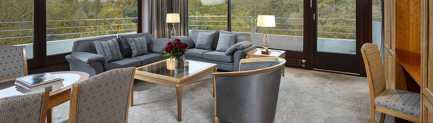 Grand Suite Living area of the Grand Suite at Maritim Hotel Kiel with large windows, stylish decor, and a view of greenery.