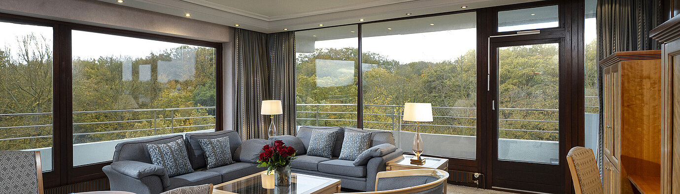 Living area of the Grand Suite at Maritim Hotel Kiel with large windows, stylish decor, and a view of greenery.