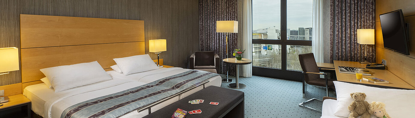 Classic family room at Maritim Hotel Düsseldorf with large double bed, single bed, playing cards, and stuffed toys for kids.