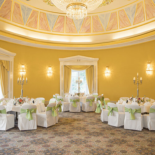Elegant ballroom with yellow walls, round tables and candle holders at Maritim Hotel Bad Wildungen