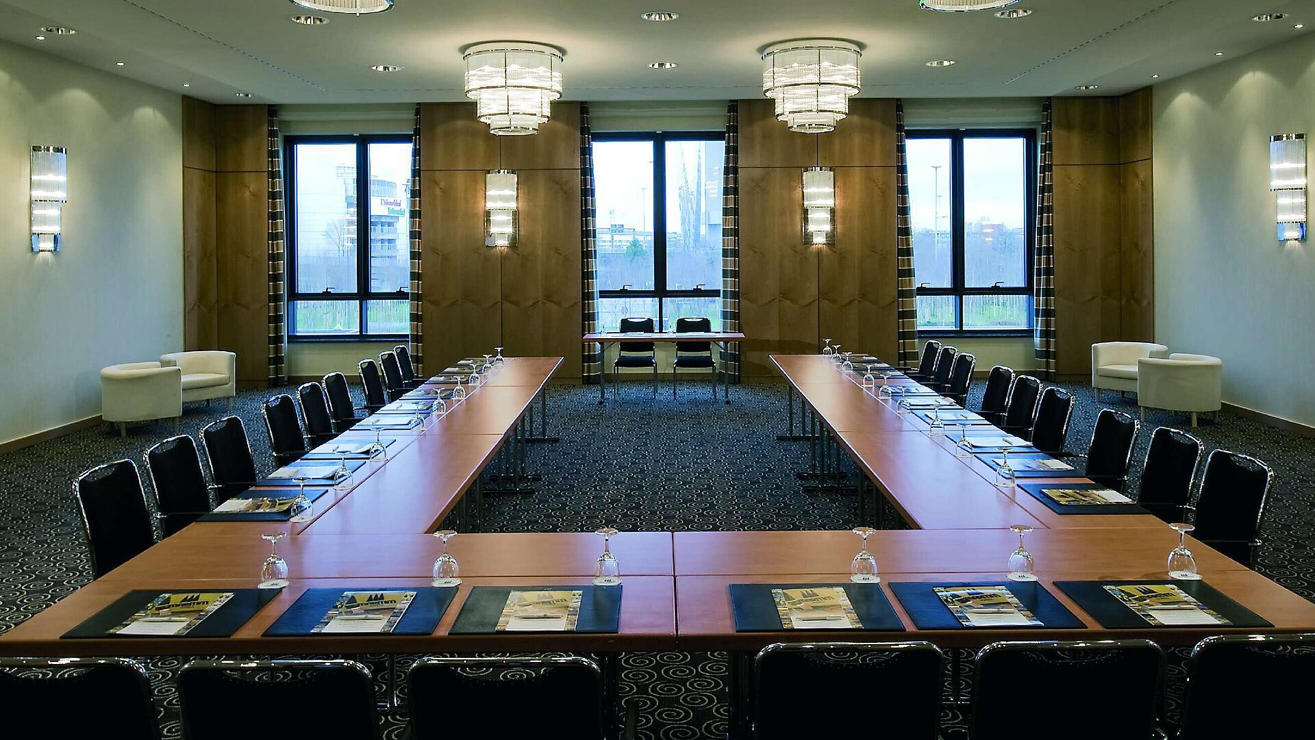 Modern conference room at Maritim Hotel Düsseldorf with U-shaped seating, large windows, and elegant lighting.