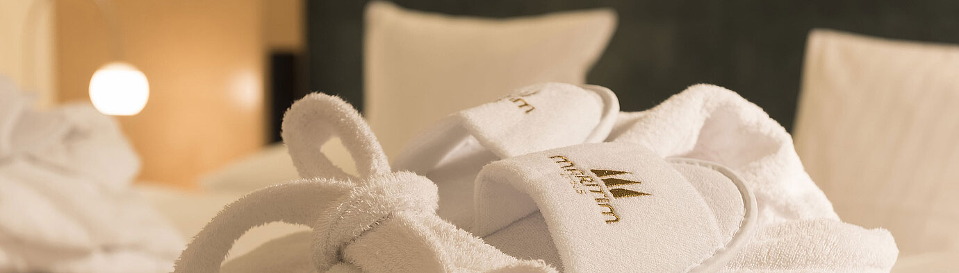 Bathrobe A fluffy bathrobe and slippers with Maritim logo on a bed at the Maritim proArte Hotel Berlin.