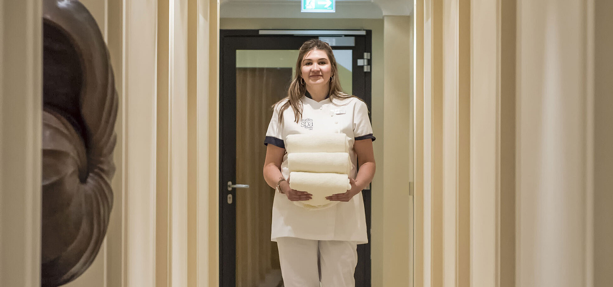 Wellness staff member in the spa area of the Maritim Hotel, carrying towels in a stylish corridor.