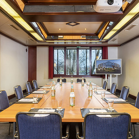 Salon Loreley, a modern conference room with square table setup, projector, and flat screen for presentations.