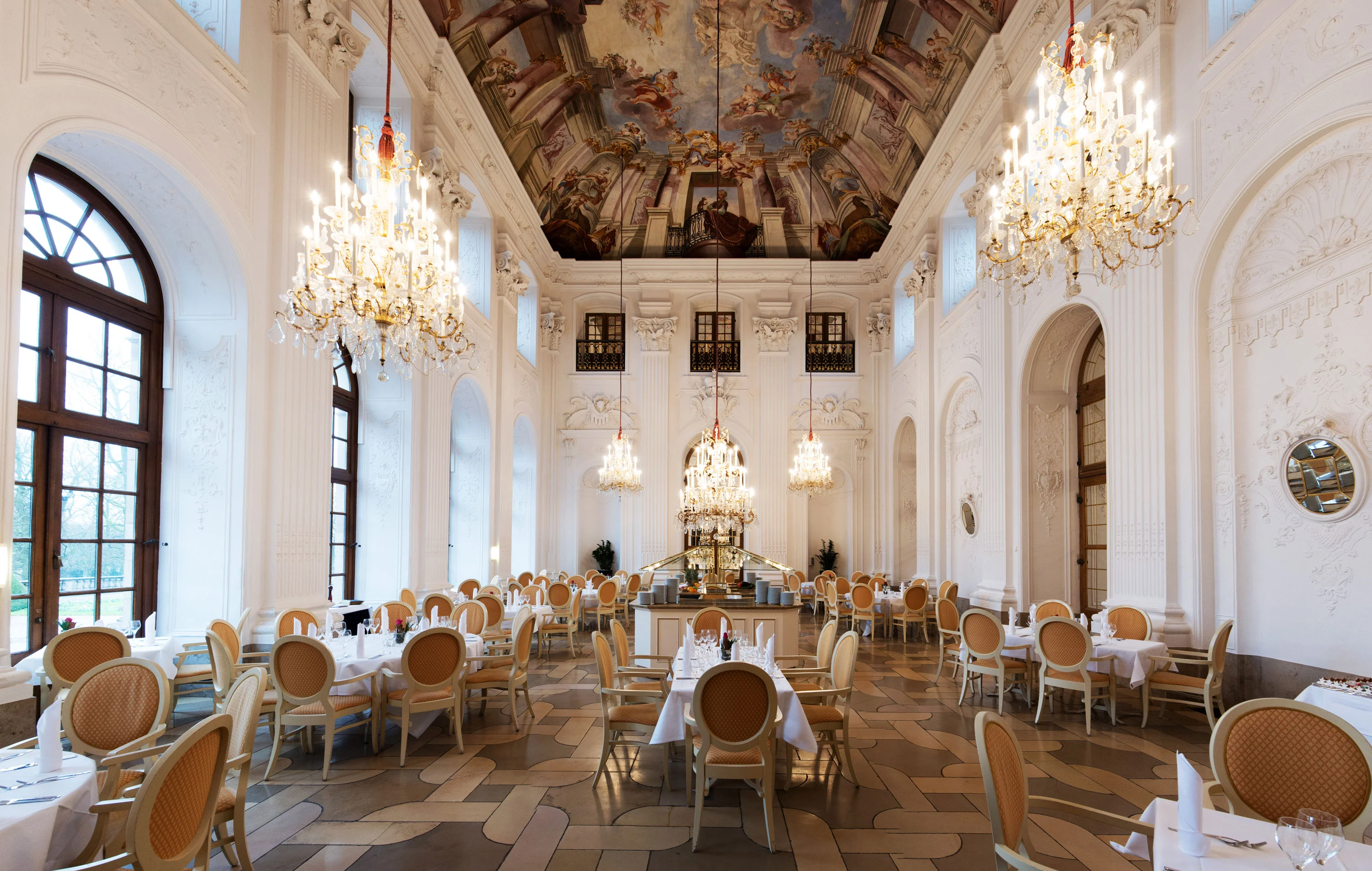 Elegant Apollo Hall at Maritim Hotel Fulda with chandeliers, fresco ceiling, and stylishly set tables.